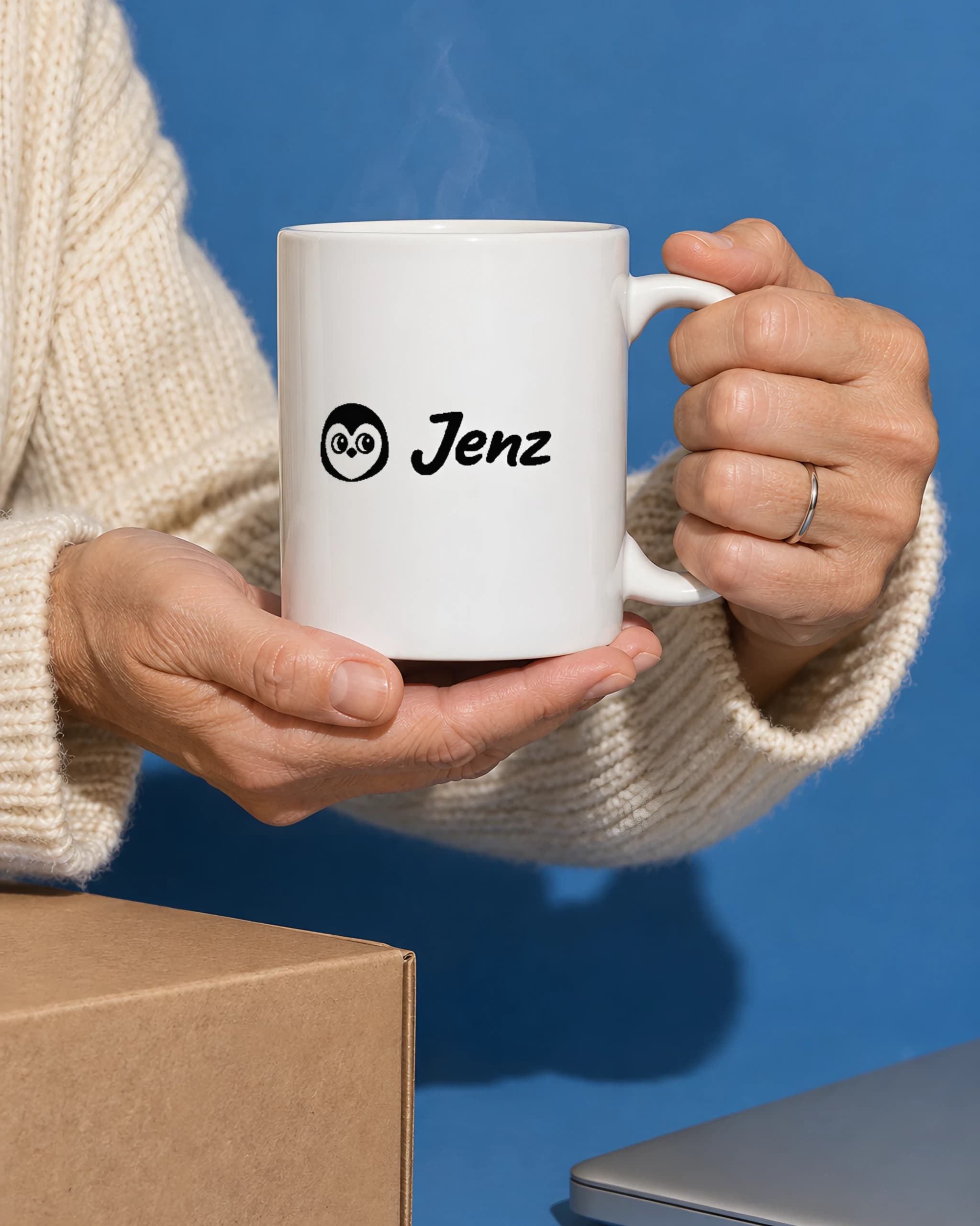 Hands in a cream knit sweater holding a white mug with a black Jenz logo