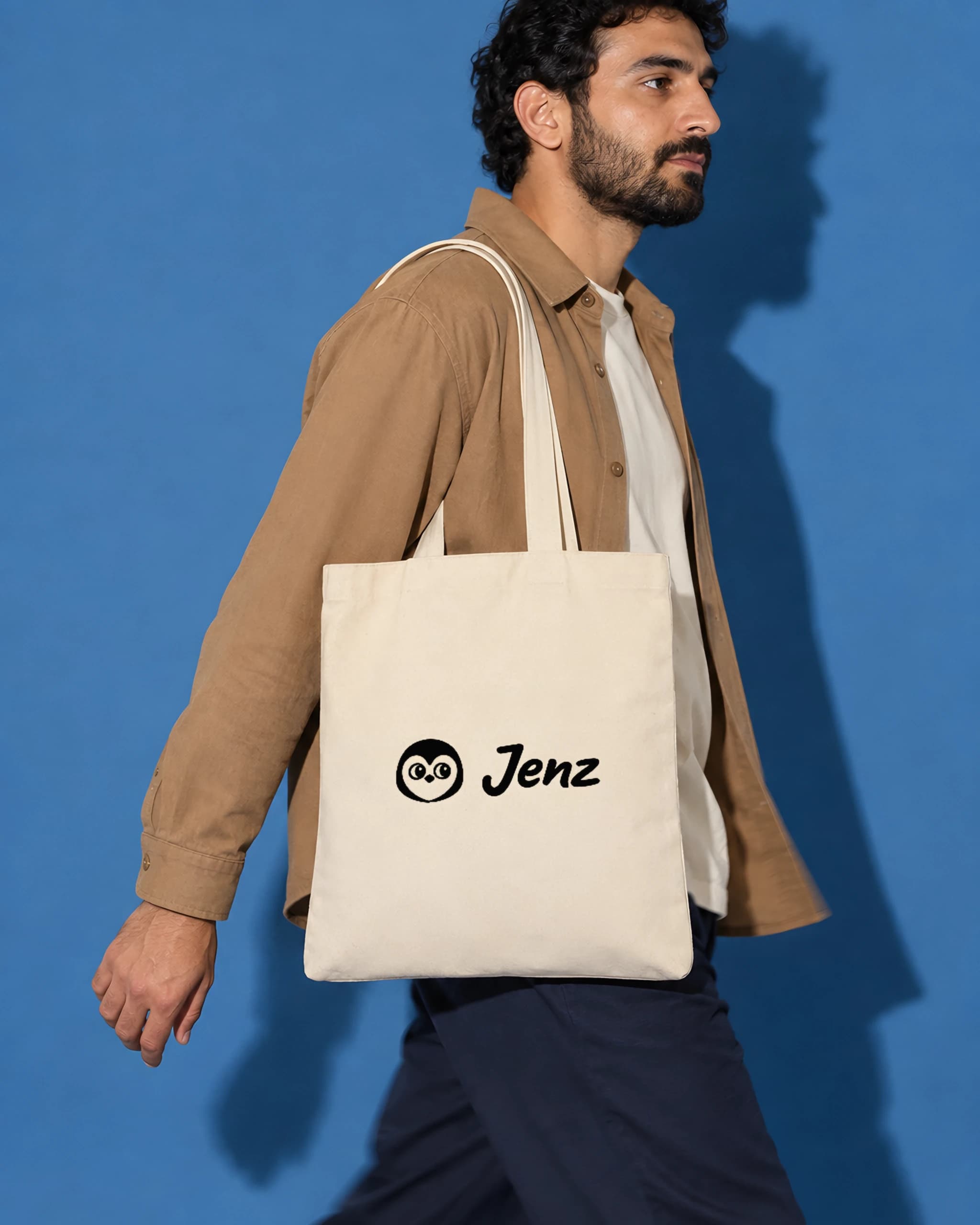 Man in a camel overshirt walking with a natural cotton tote bag with a black Jenz logo